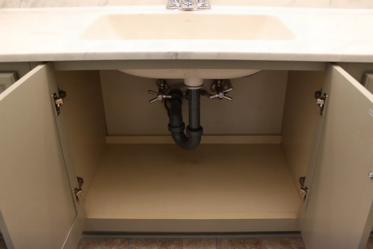 Amateur photo of a vanity sink cabinet open showing a trap and shutoff valves